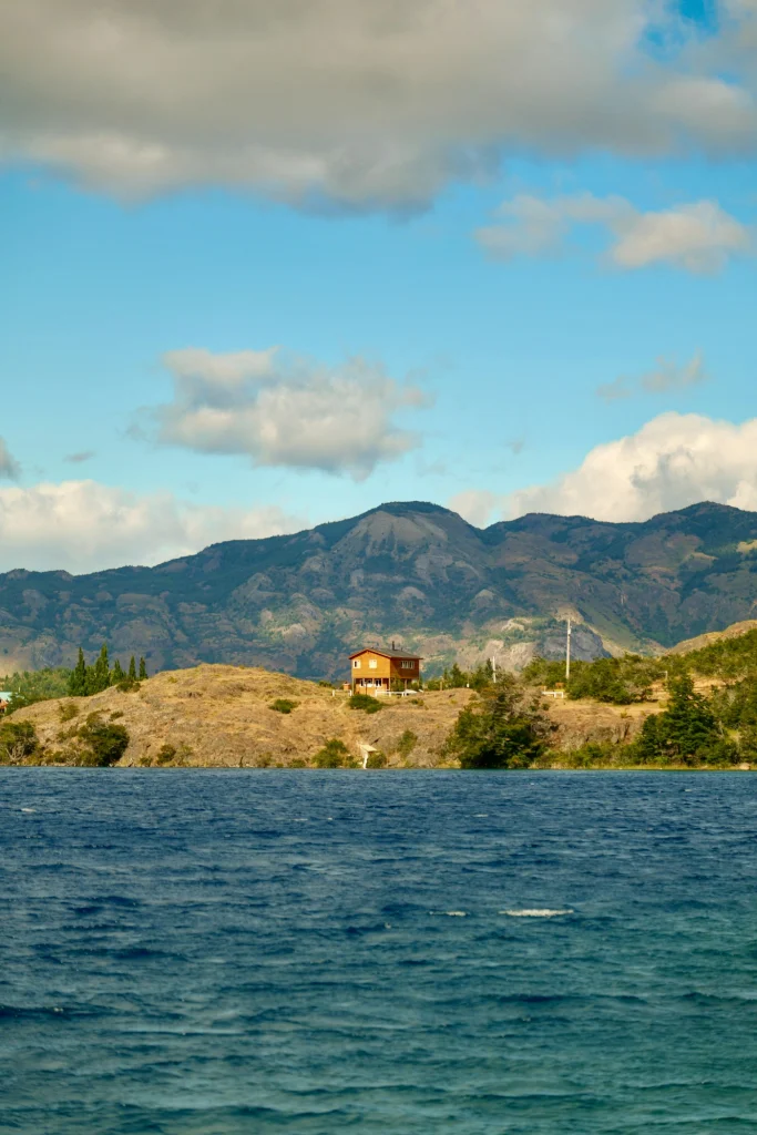 Casa de madera junto a un lago, con cerros al fondo